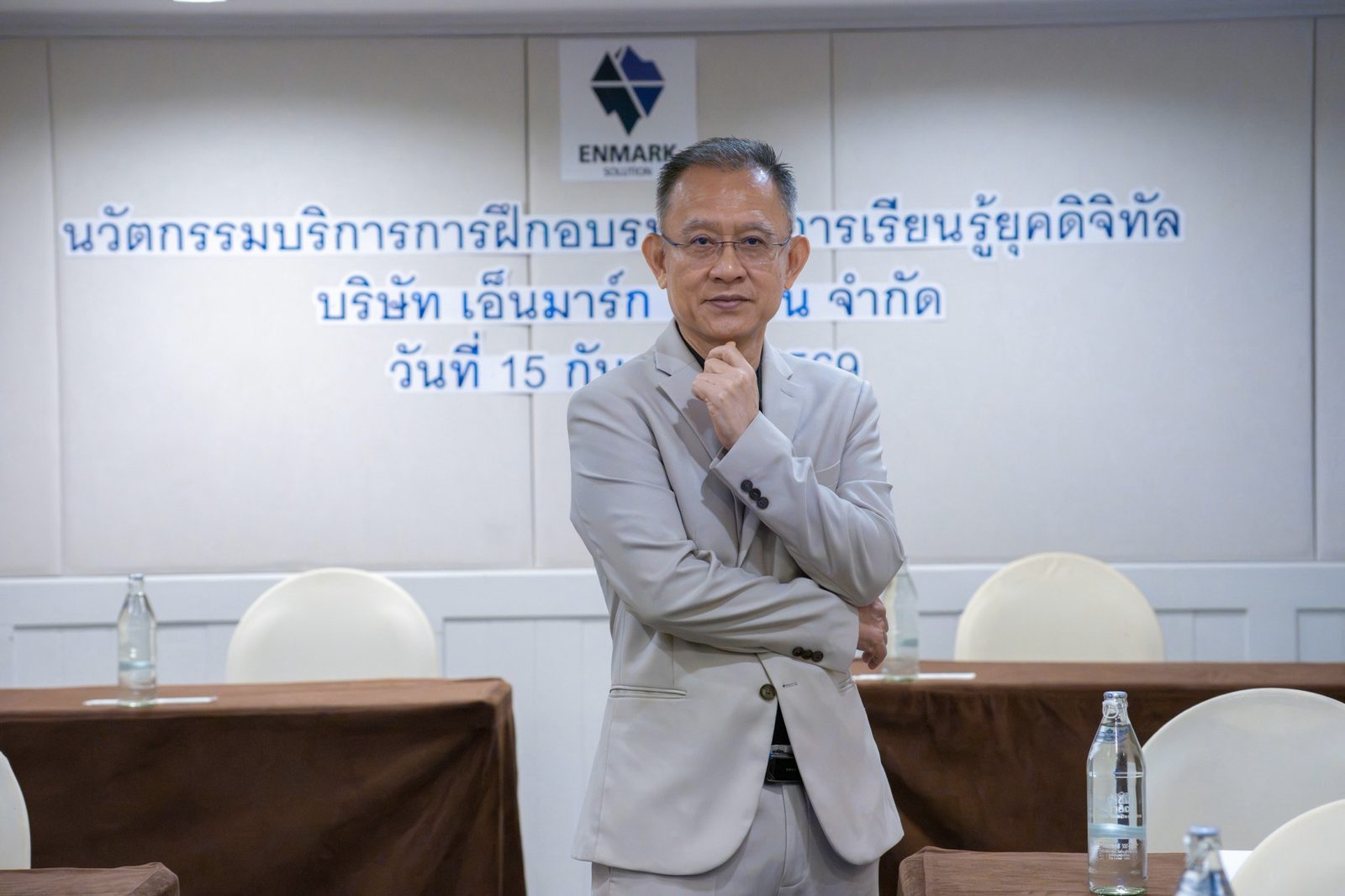 อ.ปกรณ์ วงศ์รัตนพิบูลย์ ยืนอยู่หน้าผนังโลโก้ Enmark Solution ในงานนวัตกรรมบริการการฝึกอบรม